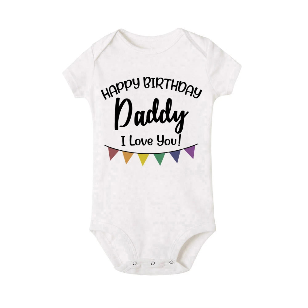 White baby bodysuit with "Happy Birthday Daddy I Love You!" text and colorful flag banner.