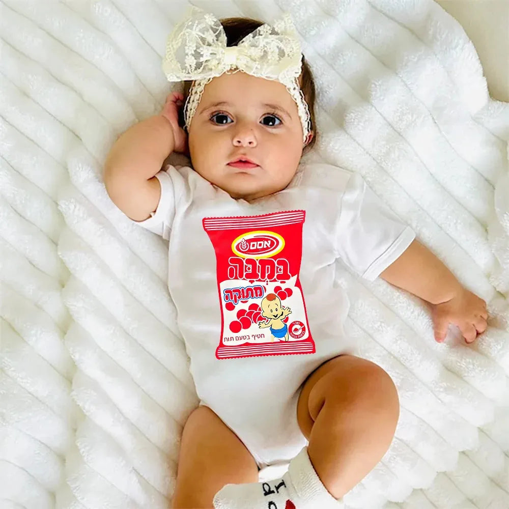 Baby in white short-sleeve bodysuit with red "Bamba" snack bag print, wearing a cream lace bow headband.