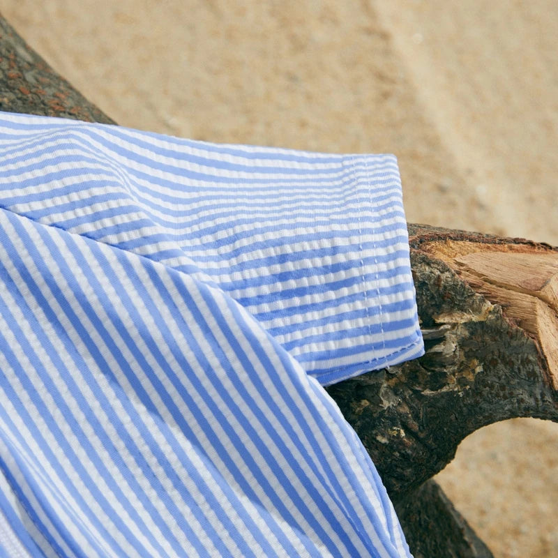 Blue and white striped short-sleeve baby swimsuit with a textured fabric, resting on a wooden log.