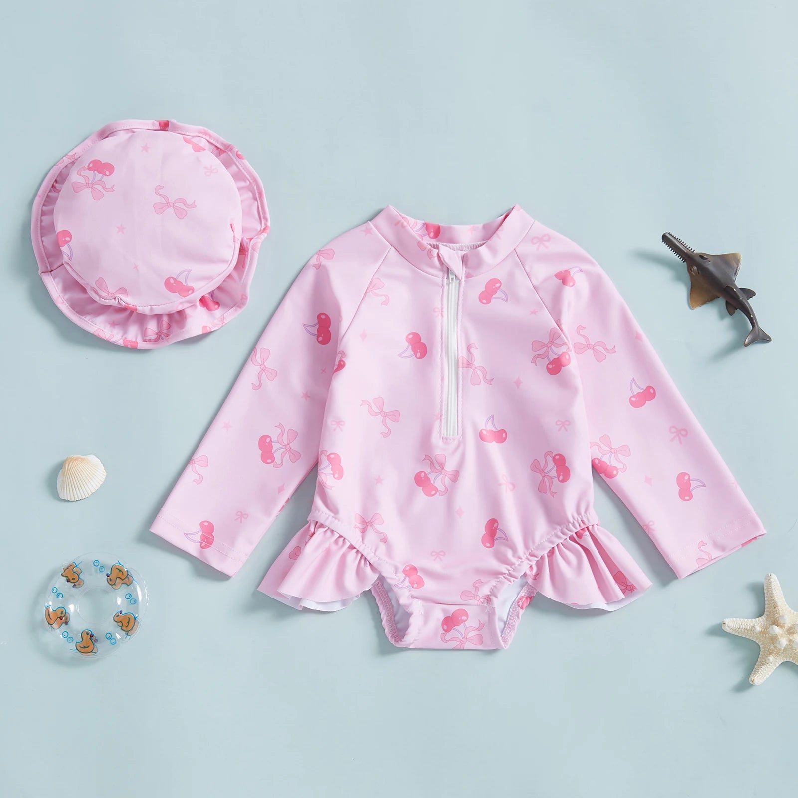 Pink long-sleeve rashguard swimsuit for babies with cherry and bow print, matching hat, and ruffles.