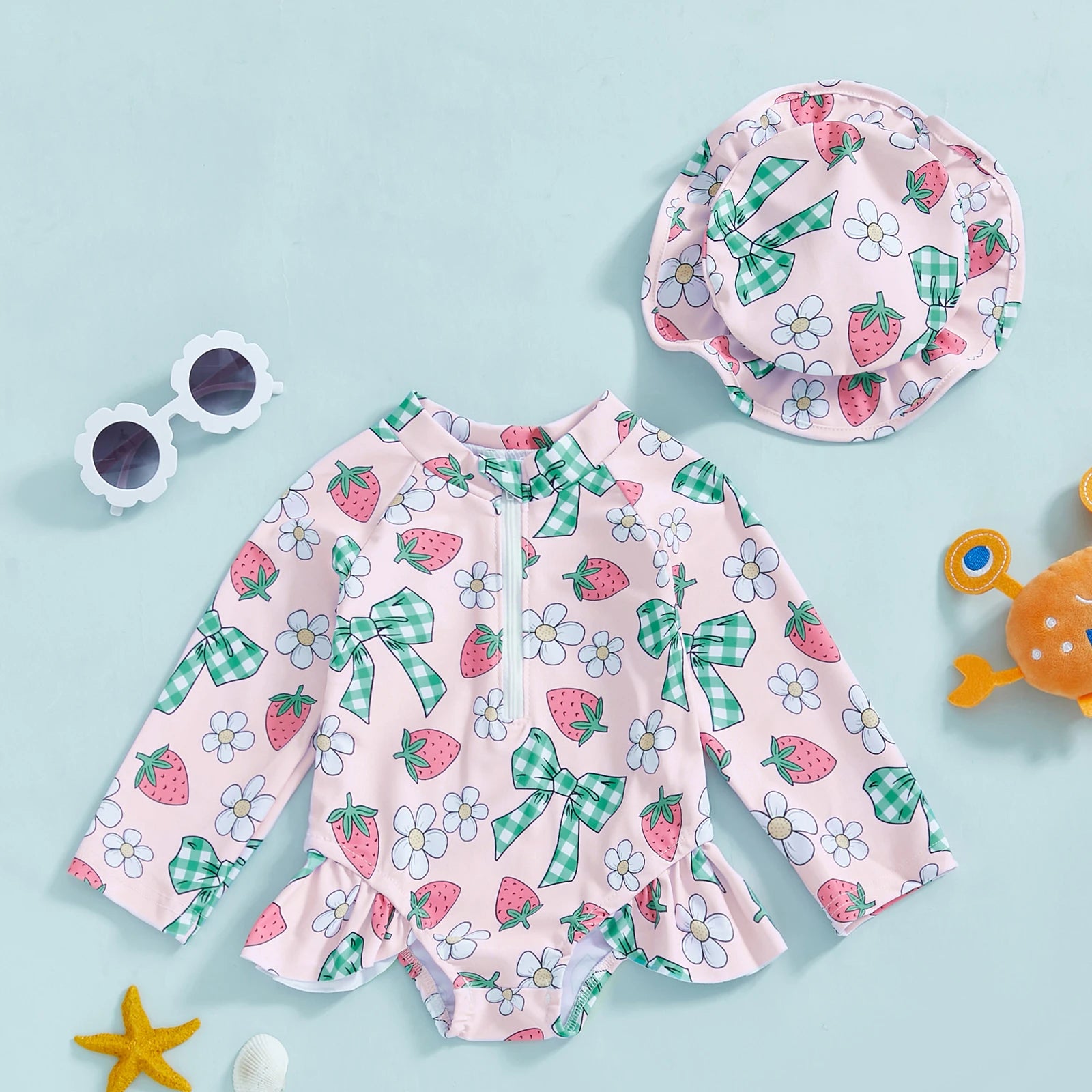 Pink long-sleeve rashguard swimsuit for babies with strawberry and bow print, matching sun hat.
