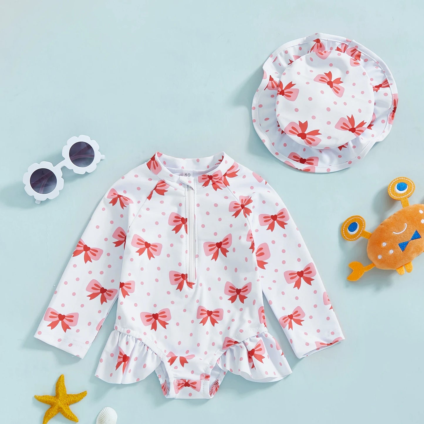 White long-sleeve rashguard swimsuit for babies with pink bows, matching sun hat, and zipper.