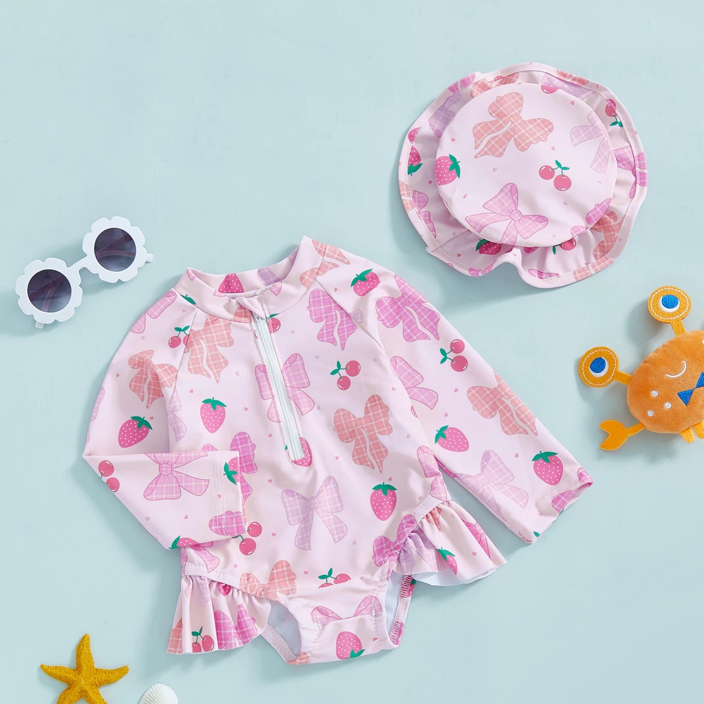 Pink long-sleeve rashguard swimsuit for babies with bow and strawberry print, matching hat, and front zipper.