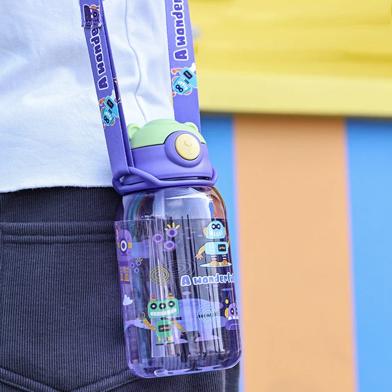 Purple kids' water bottle with straw, handle, and robot design, hanging from a colorful strap.