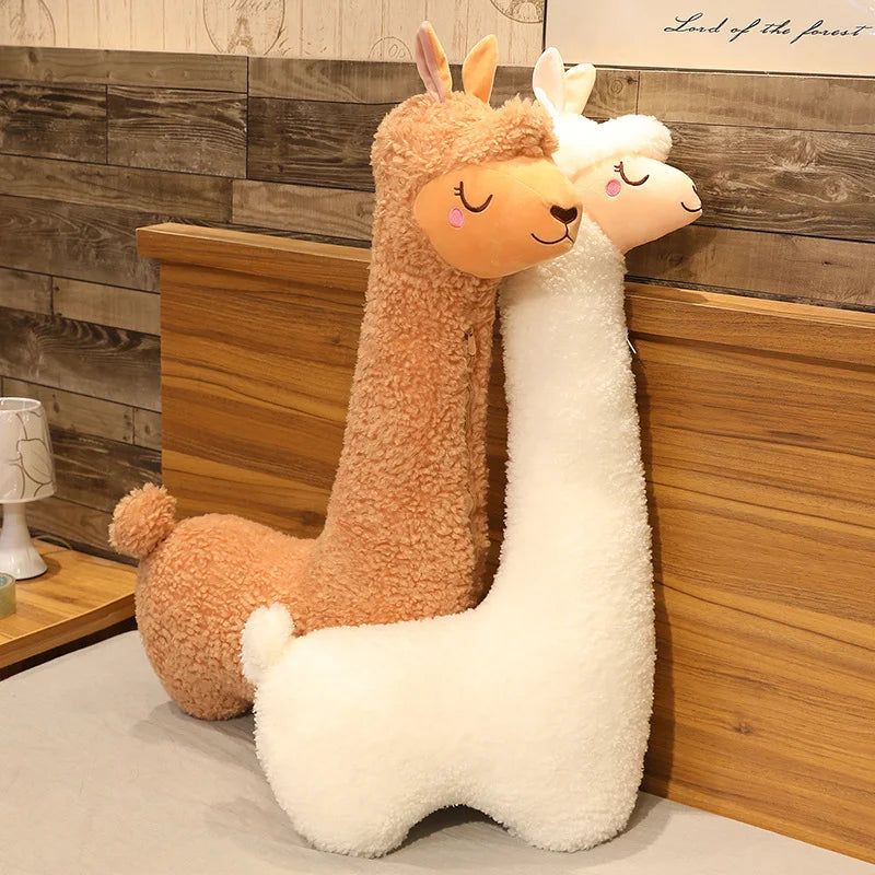 Two soft plush alpaca pillows, one brown and one white, with long necks, on a bed.