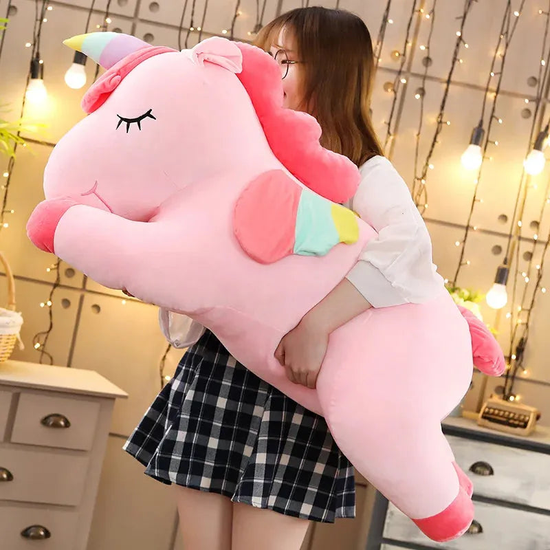Large pink plush unicorn toy with rainbow horn and wings, held by a person.