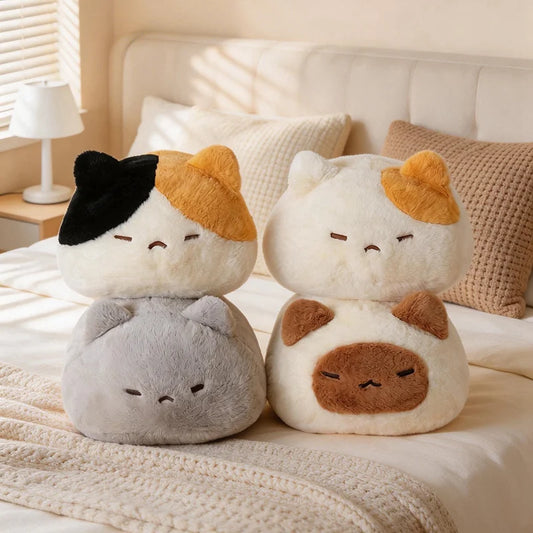 Four soft, plush cat pillows in various colors (calico, white/orange, gray, white/brown) on a bed.