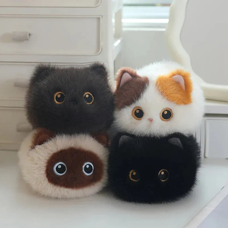 Four soft, round plush cat toys in black, white/brown/orange, cream/brown, and black, with big eyes.