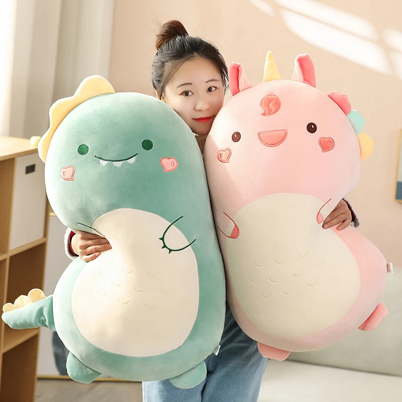 Woman holding a large green dinosaur and pink unicorn plush pillow, soft velvet material.
