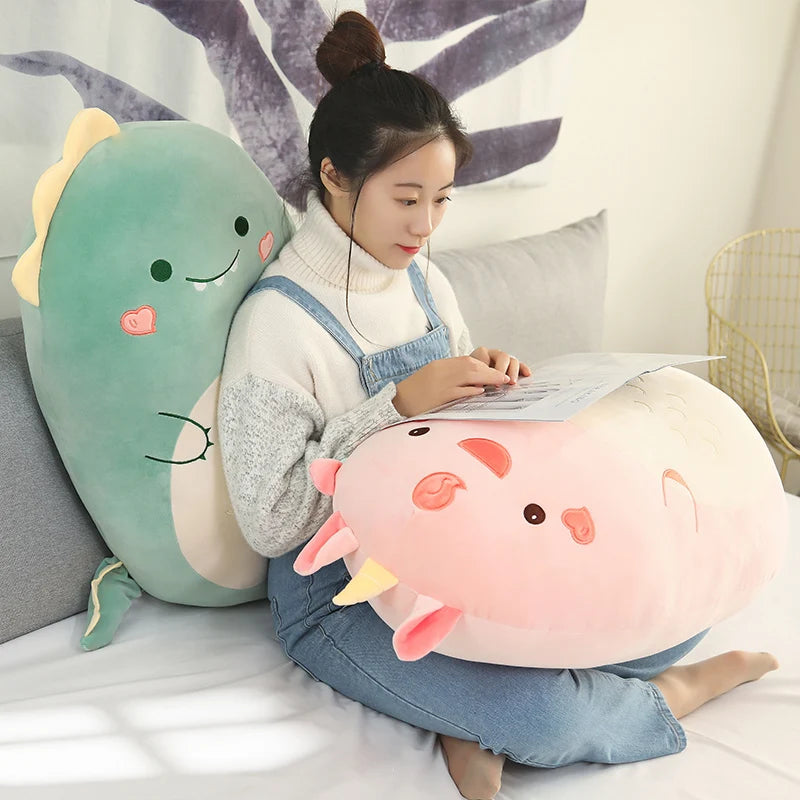Woman holding a soft pink plush animal pillow, with a large green dinosaur plush behind her.