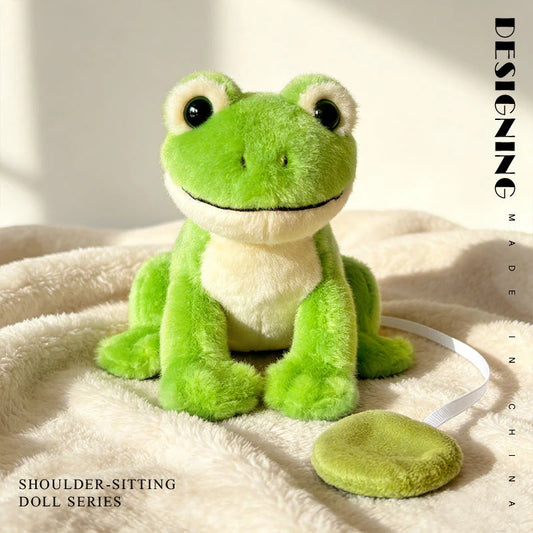 Green plush magnetic frog shoulder doll with white belly and black eyes, sitting on a soft blanket.