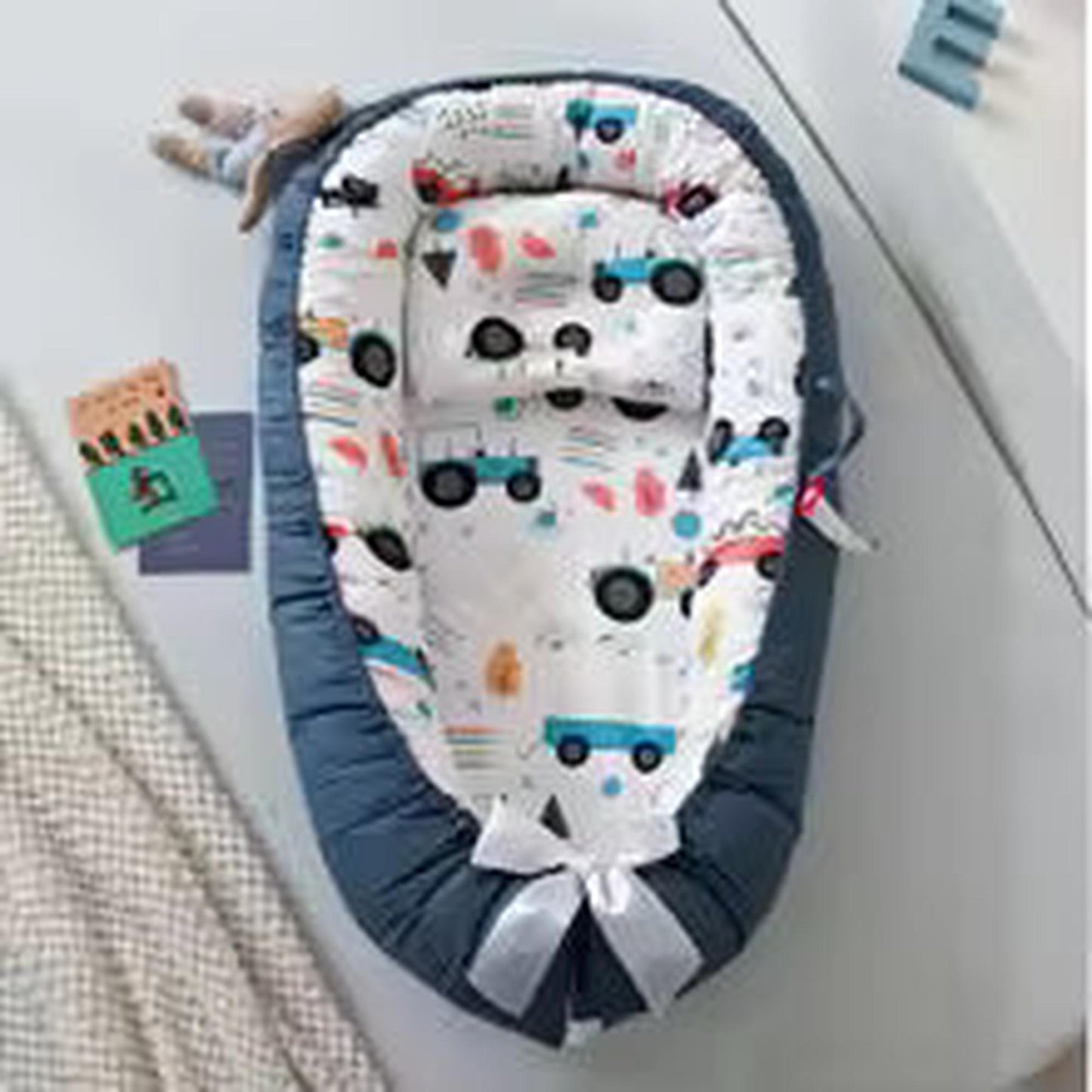 Adjustable baby nest in blue with a white cotton insert featuring colorful vehicle patterns.