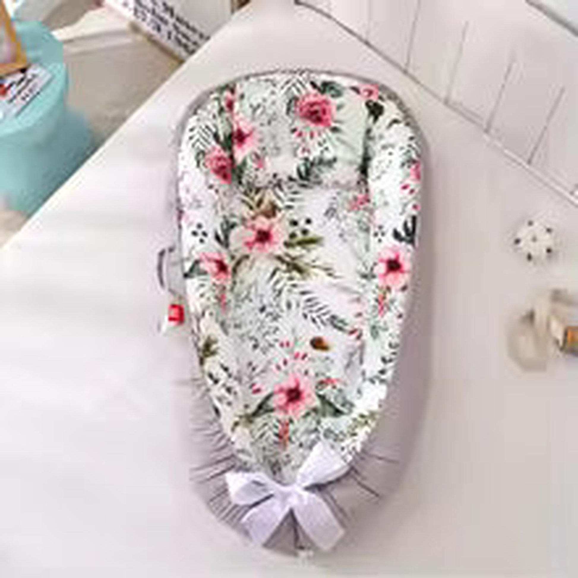 Adjustable baby nest with white floral print, pink roses, and gray base with white bow.