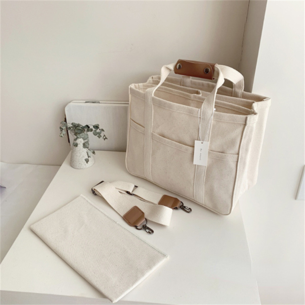 Beige canvas diaper bag with brown leather accents, multiple pockets, detachable strap, and matching pouch.