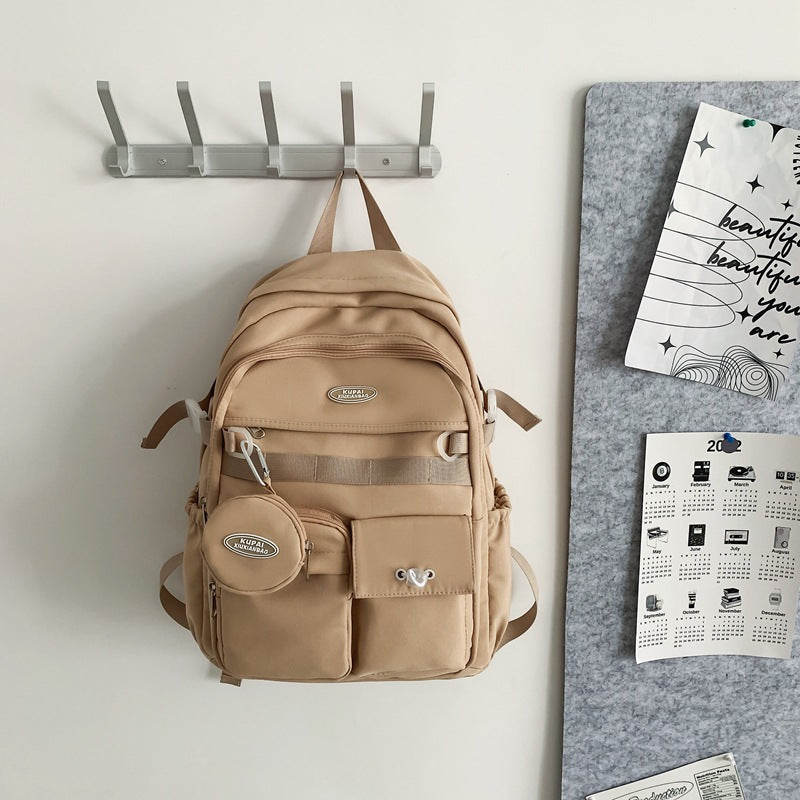 Beige nylon student backpack with laptop compartment, multiple pockets, and a small round pouch.