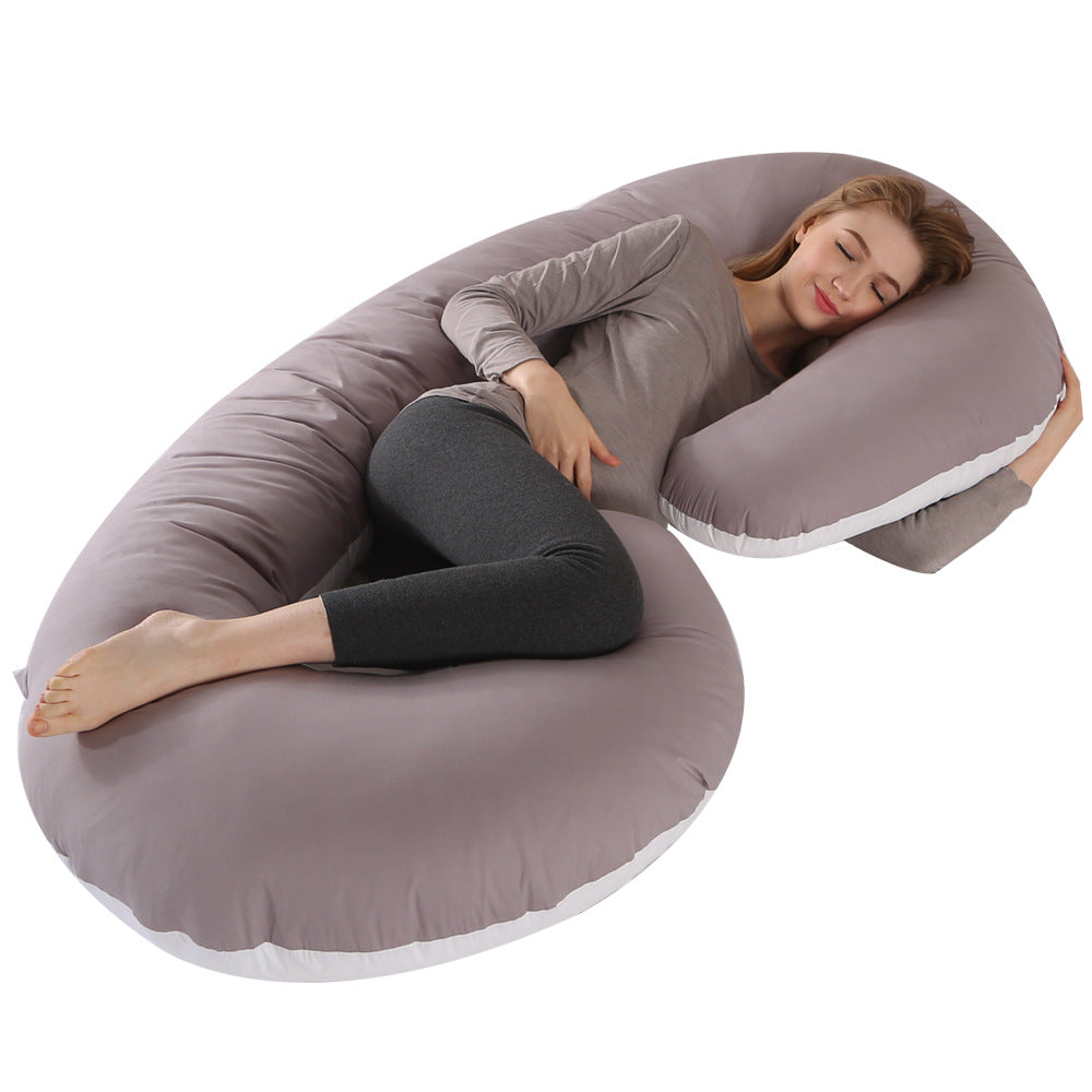 Pregnant woman sleeping soundly on a large gray C-shaped velvet maternity pillow with white trim.