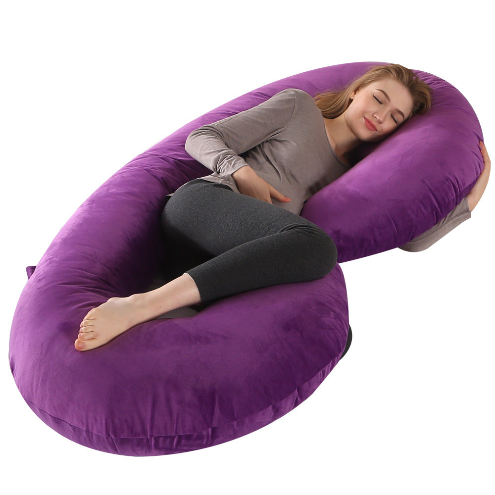 Pregnant woman sleeping peacefully on a large purple velvet C-shaped maternity pillow.