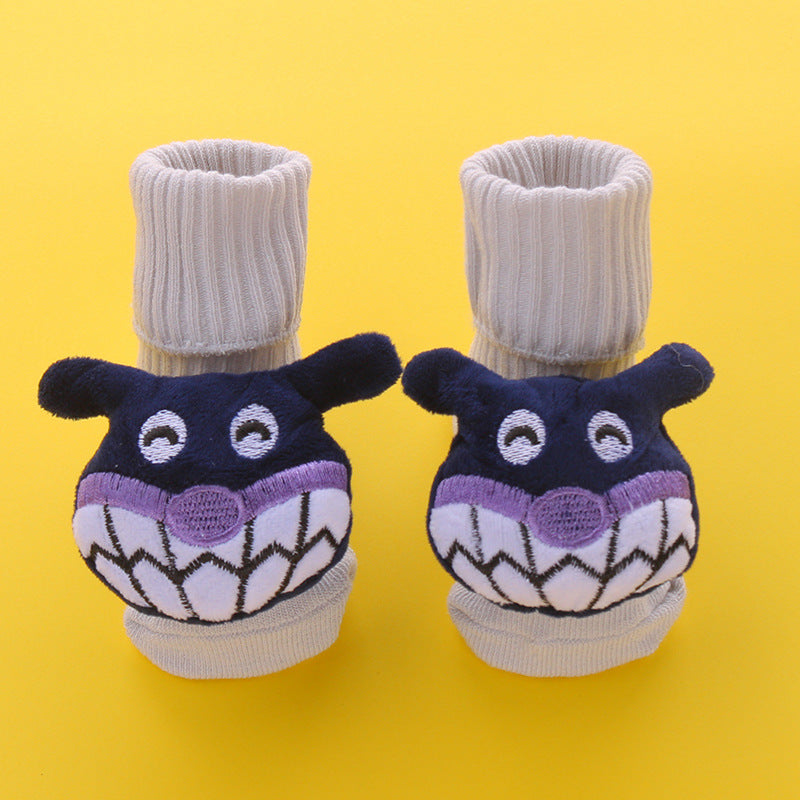 Pair of beige cotton baby socks with purple monster faces and anti-slip soles.