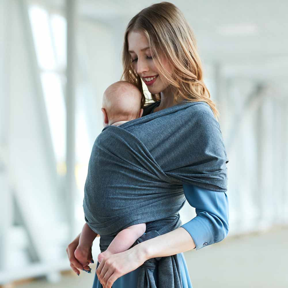 Smiling woman cradling a baby in a soft, dark gray cotton fabric baby wrap carrier.