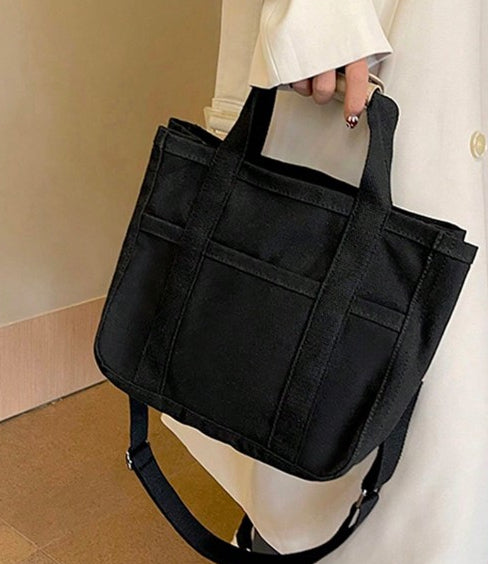 Black canvas multi-functional diaper bag with top handles, shoulder strap, and multiple exterior pockets.