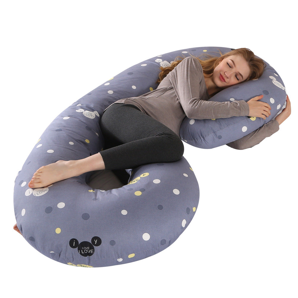 Pregnant woman sleeping soundly on a large C-shaped gray velvet maternity pillow with white and yellow polka dots.