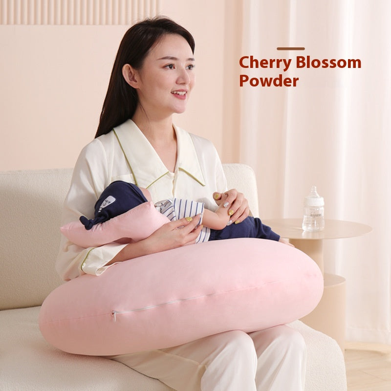 Smiling woman cradling baby on a pink cherry blossom powder nursing pillow.