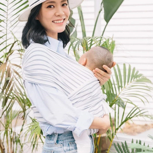 Smiling woman wearing a white and grey striped X-Type ergonomic baby carrier with a sleeping infant.