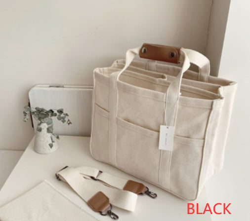 Cream canvas diaper bag with brown leather accents, multiple pockets, and a detachable shoulder strap.