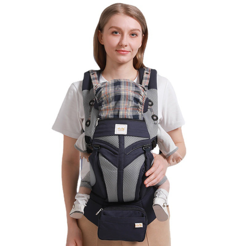 Woman wearing a navy ergonomic cotton baby carrier with plaid accents and a front pouch.
