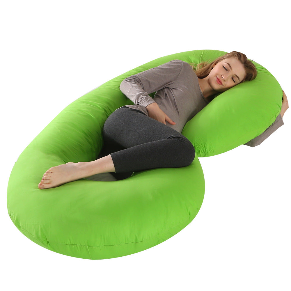 Pregnant woman sleeping comfortably on a large, bright green C-shaped velvet maternity pillow.