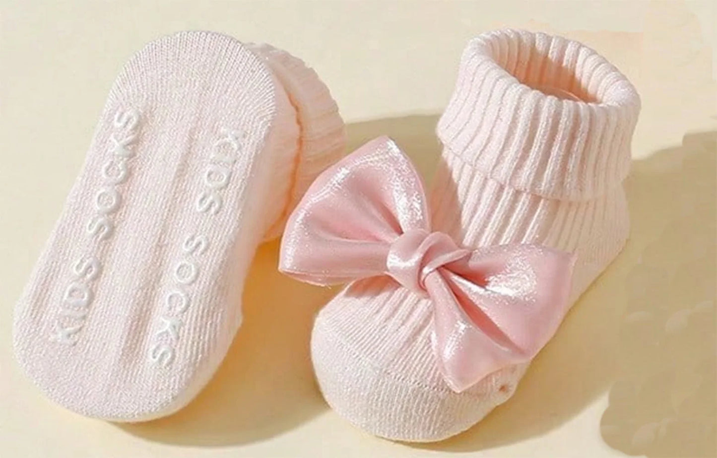 Pink cotton baby socks with large satin bows and anti-slip soles.