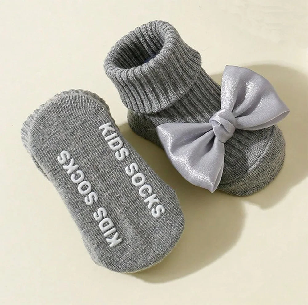 Gray cotton baby socks with large satin bows and anti-slip "KIDS SOCKS" grip on soles.