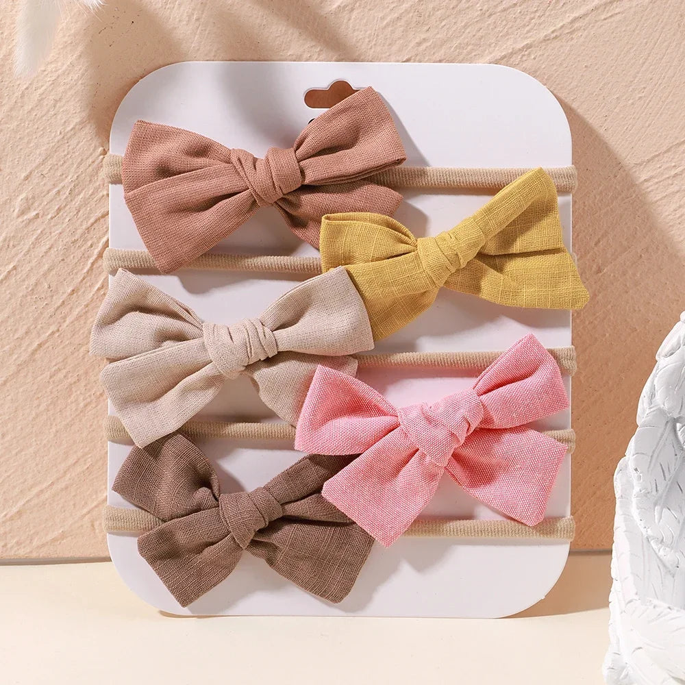 Set of 5 baby headbands with soft fabric bows in pink, yellow, beige, brown, and blush.