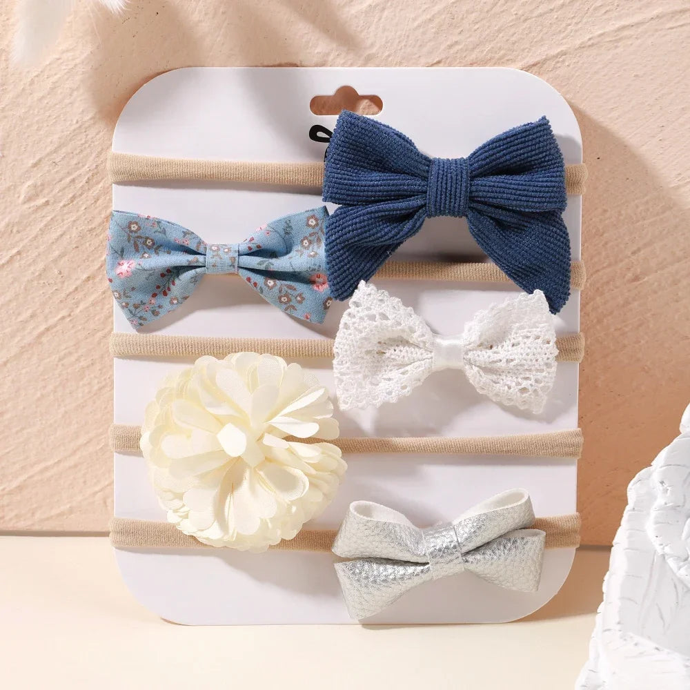 Set of 5 baby headbands with floral, lace, corduroy, and metallic bows in blue, white, and silver.