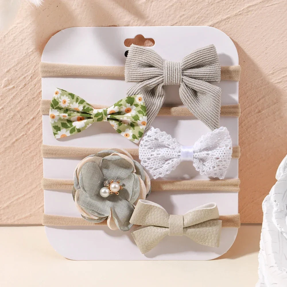 Set of 5 baby headbands with varied designs: ribbed bow, floral bow, lace bow, fabric flower with pearls, and faux leather bow.