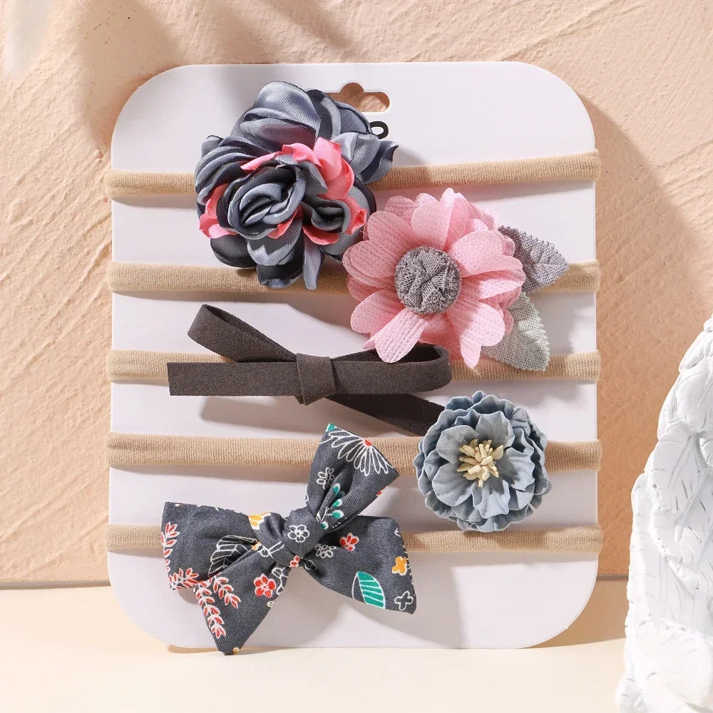 Set of 5 baby headbands with lace flowers and bows in pink, gray, and floral patterns.