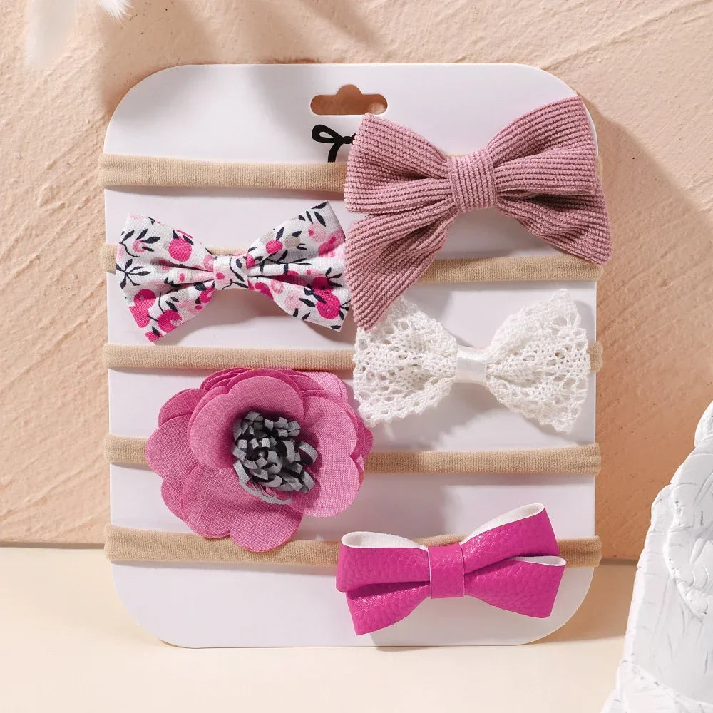 Set of 5 baby headbands: pink ribbed bow, floral bow, white lace bow, pink fabric flower, and fuchsia leatherette bow.