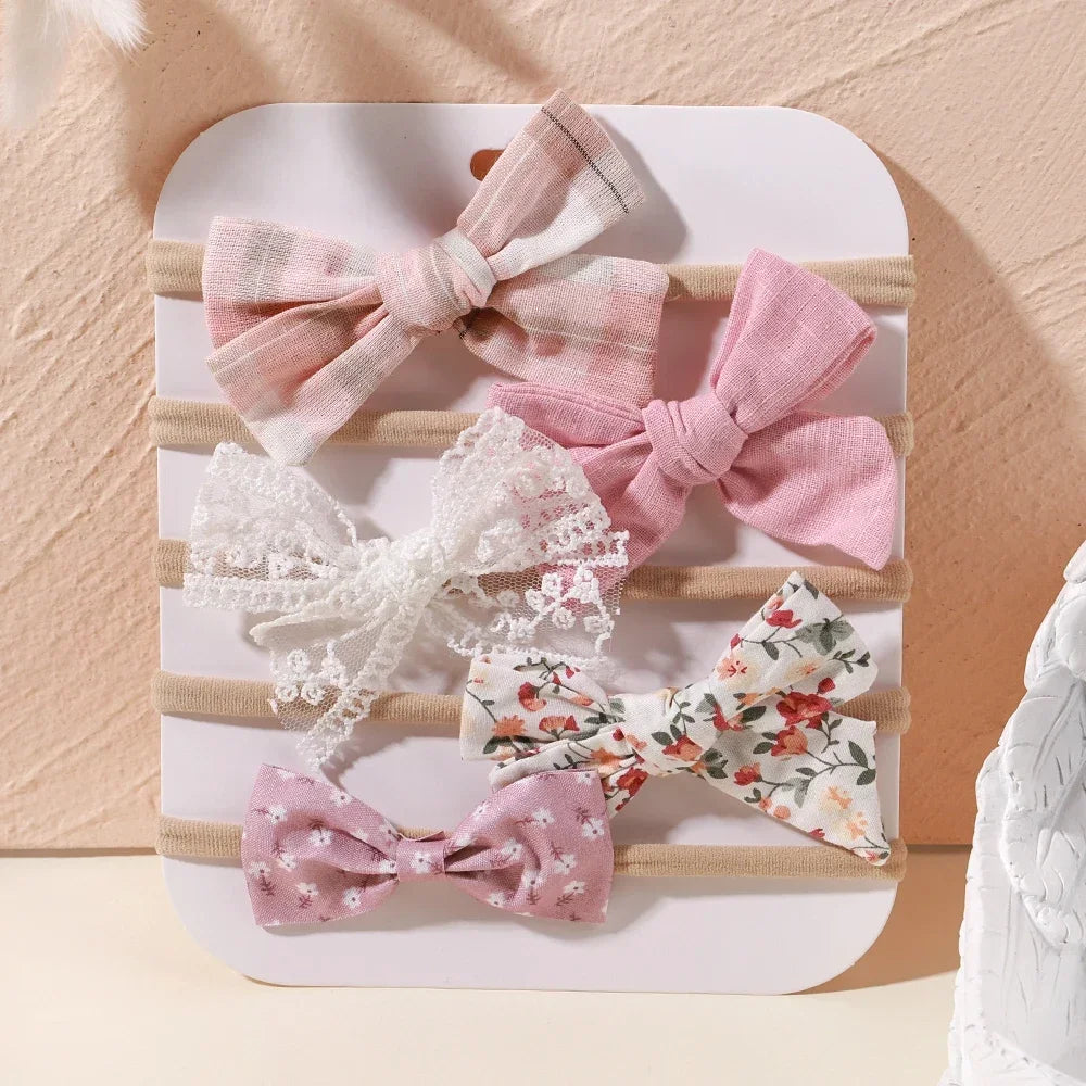Set of 5 baby headbands with pink, white lace, and floral bow designs on soft nylon.