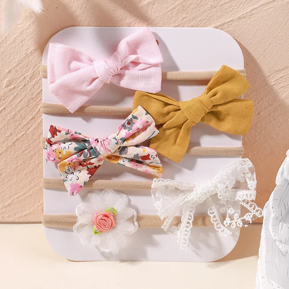Set of 5 baby headbands: pink, mustard, floral bow, white lace bow, and white flower.