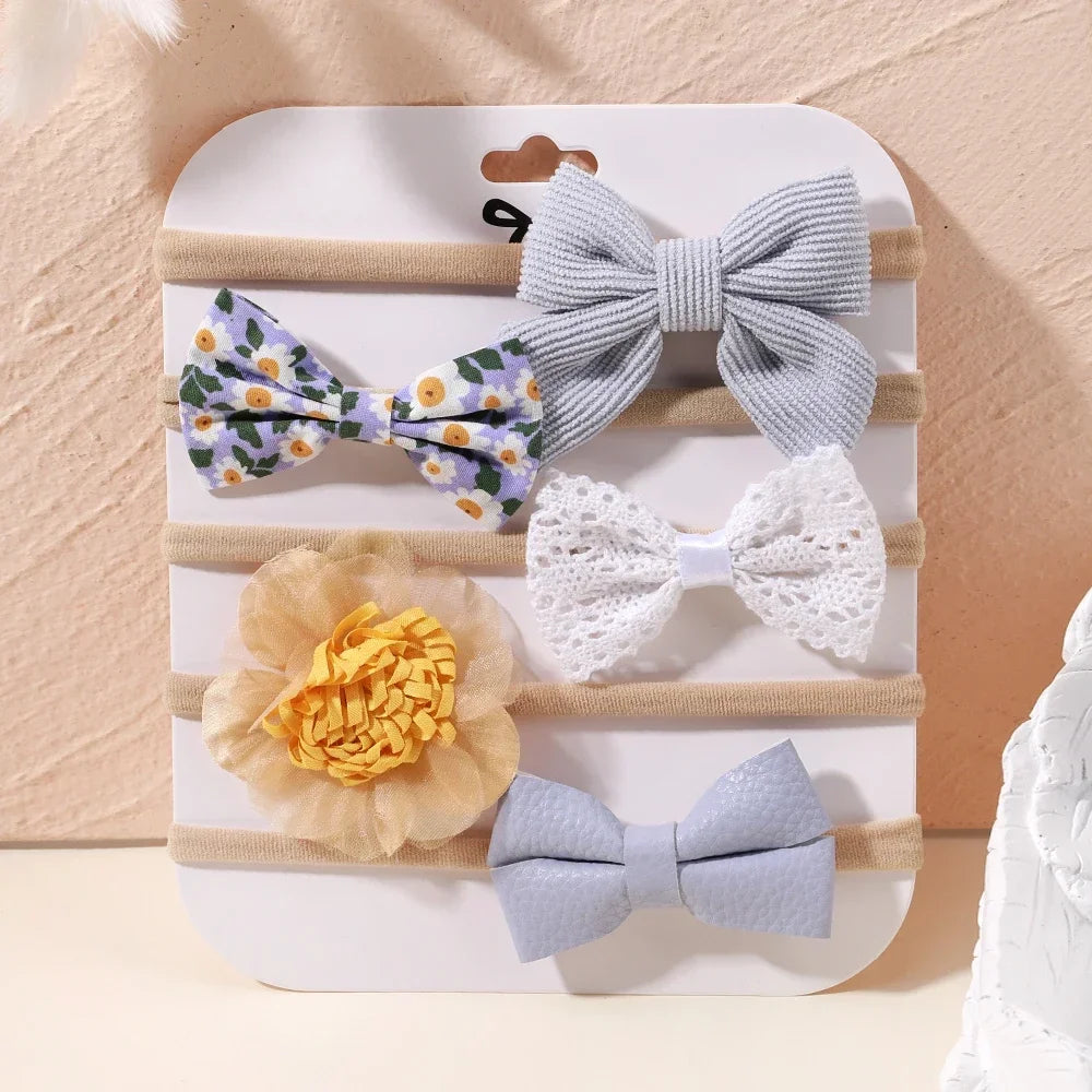 Set of 5 baby headbands with various lace, floral, and bow designs in soft pastel colors.