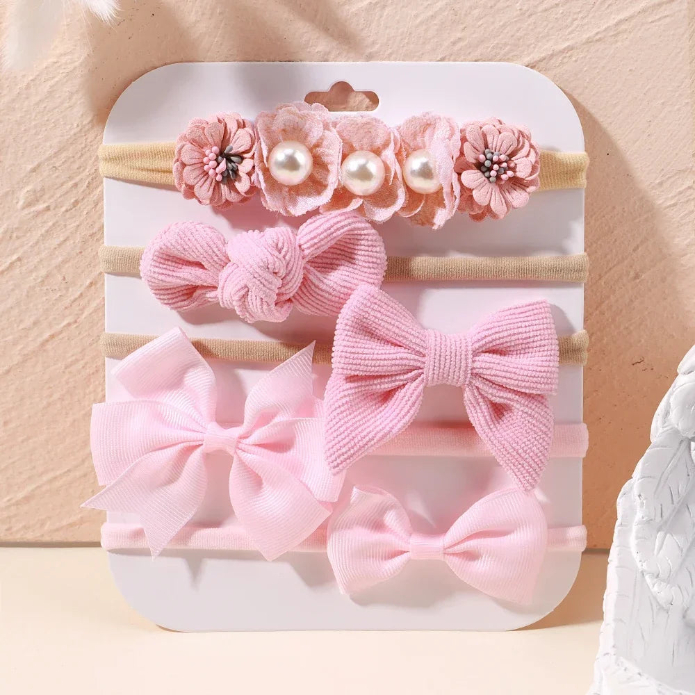 Set of 5 pink baby headbands: floral lace, pearl, corduroy, and satin bows on soft nylon.