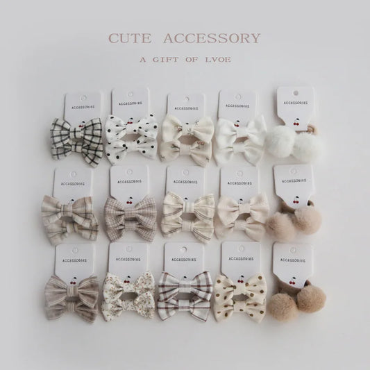 Set of 10 handmade elastic hair bows for girls in various patterns: plaid, polka dot, floral, and solid cream, plus two pom-pom ties.