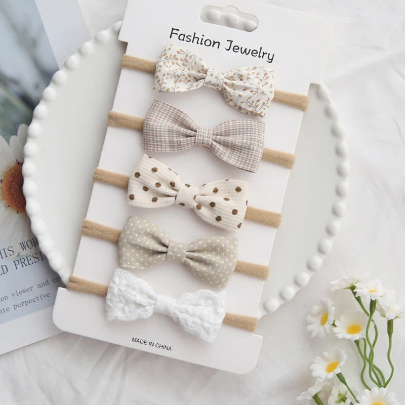 Set of five soft cotton baby headbands with assorted patterned bows in neutral colors.