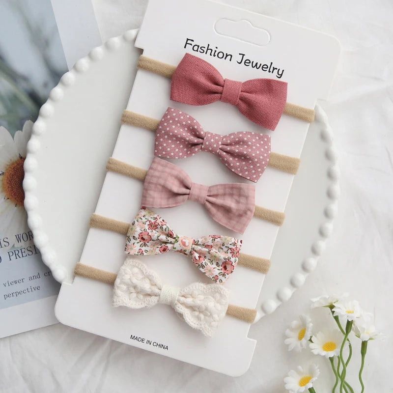 Set of 5 baby headbands with handmade bows in pink, floral, and cream textures.