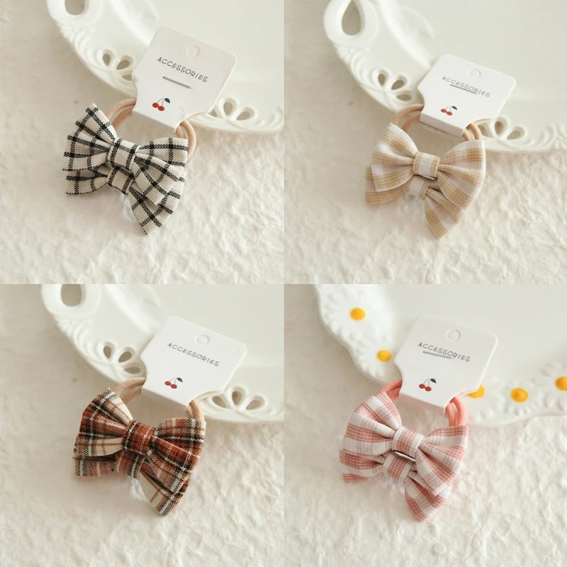 Four plaid cotton hair bows for babies and girls in black, tan, brown, and pink, on soft elastic bands.
