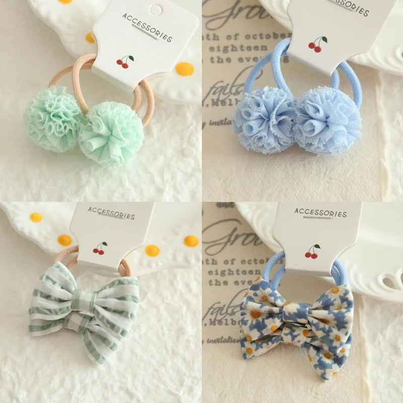 Four sets of soft hair ties for babies and girls: two with fluffy pom-poms (mint and blue), and two with fabric bows (striped green and floral blue).