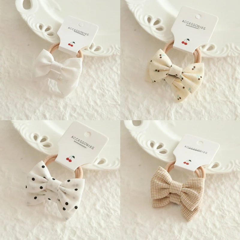 Four soft cotton hair bows for babies and girls: solid white, cream with cherries, white with black polka dots, and beige plaid.
