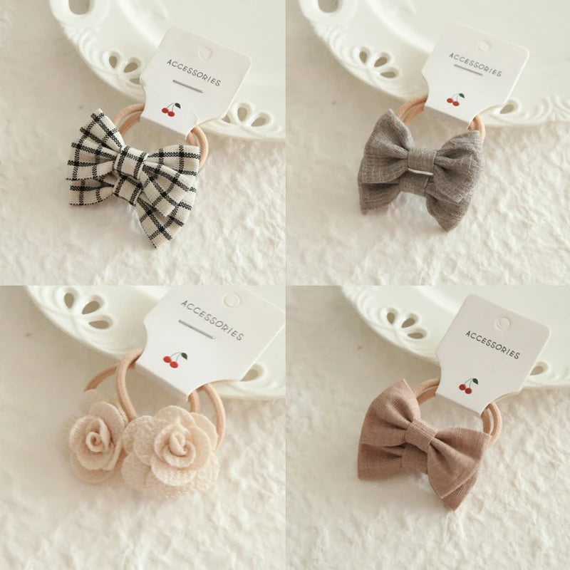 Four soft cotton hair ties for babies and girls: plaid bow, gray bow, two beige roses, and a pink bow.