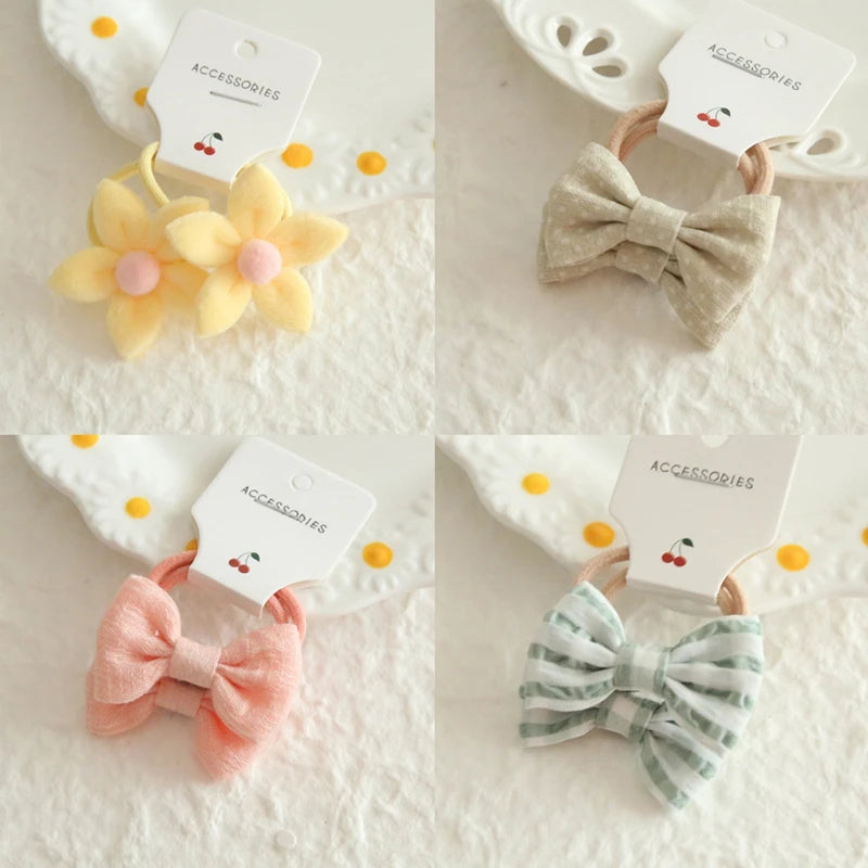 Four soft cotton hair ties for babies and girls: yellow flowers, beige polka dot bow, pink bow, and green striped bow.