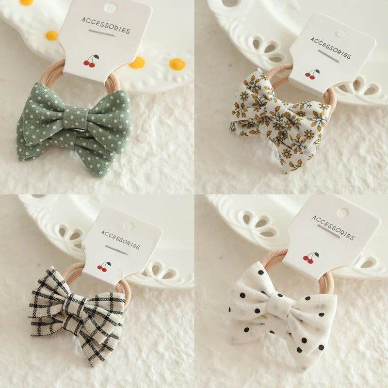 Four soft cotton hair ties for babies and girls, featuring bow designs in polka dot green, floral, plaid, and polka dot white.